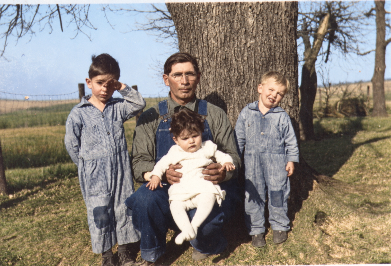 Colorized family photograph of a father seated with three children beside a tree